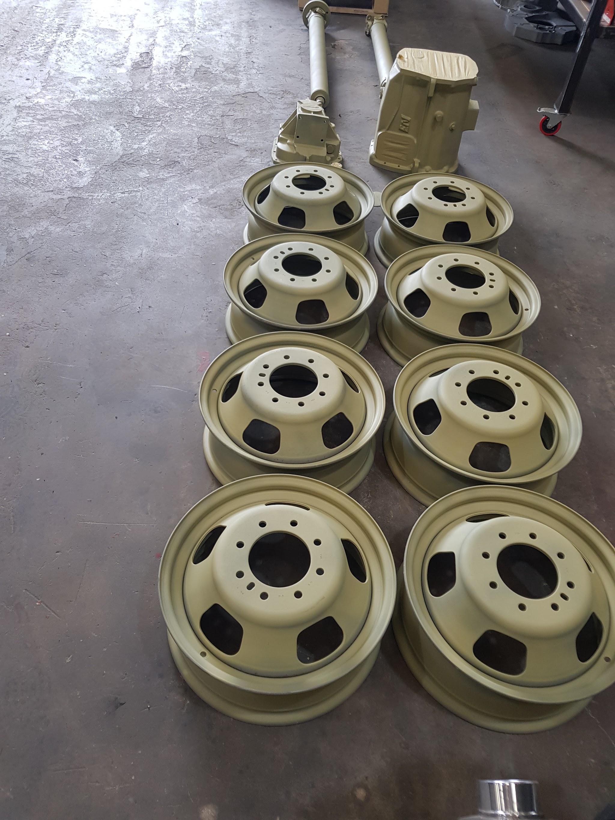 Eight commercial-vehicle steel wheels refinished in sand beige, laid out on the workshop floor