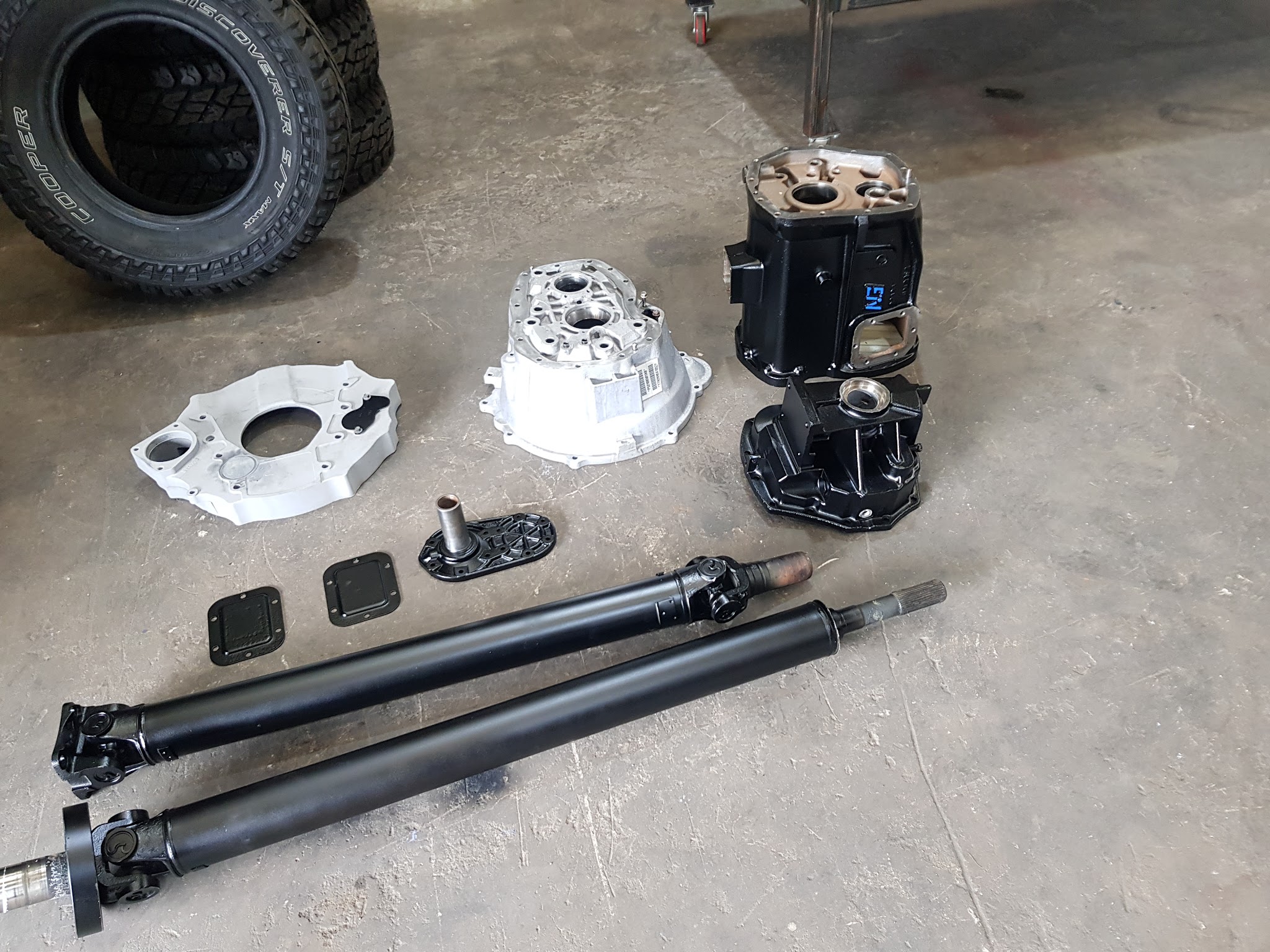Drivetrain parts laid out on the workshop floor: adaptor plate, bellhousing, gearbox casings and two propshafts