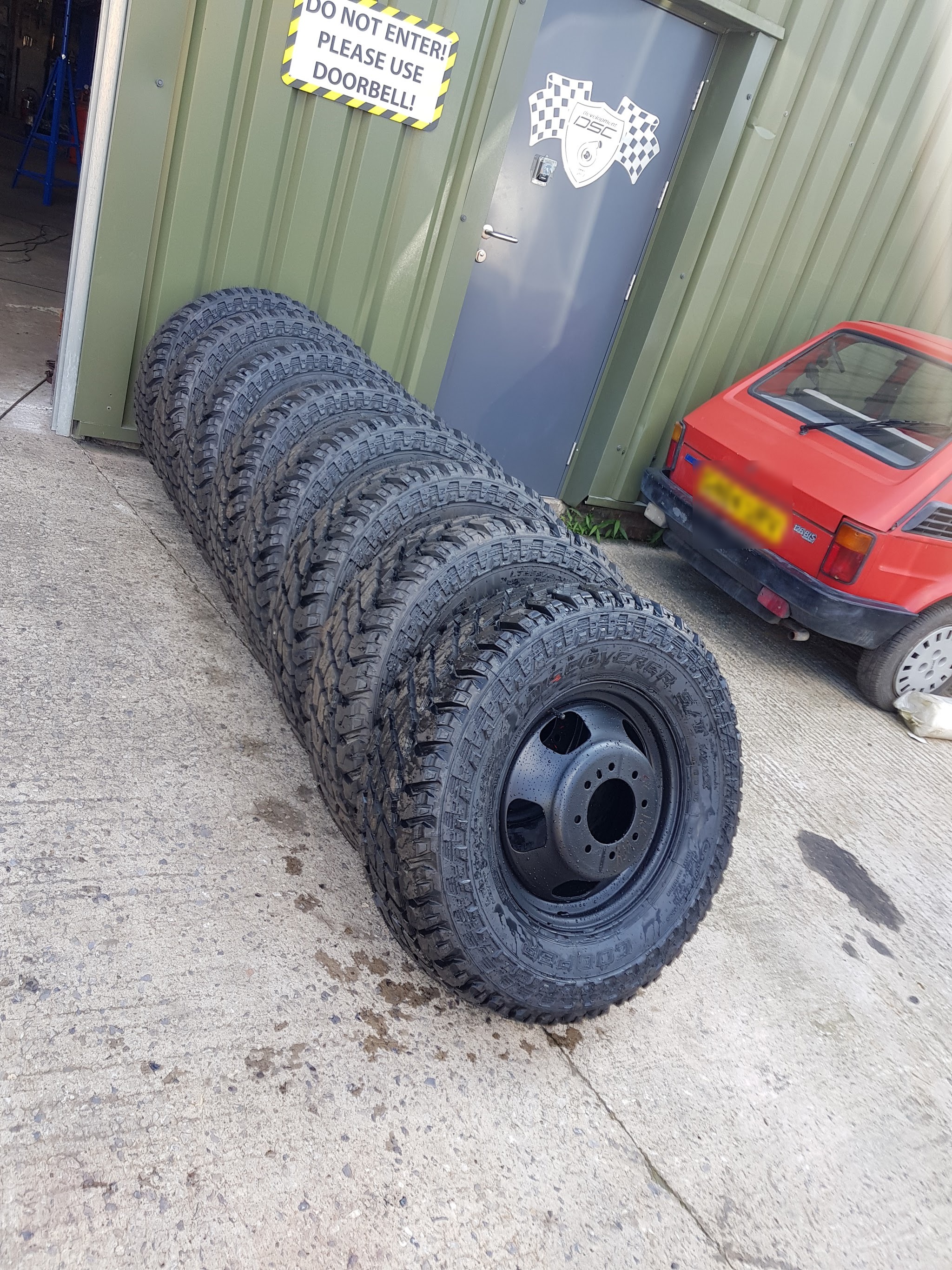 A row of all-terrain tyres on black steel wheels outside the DSC unit door